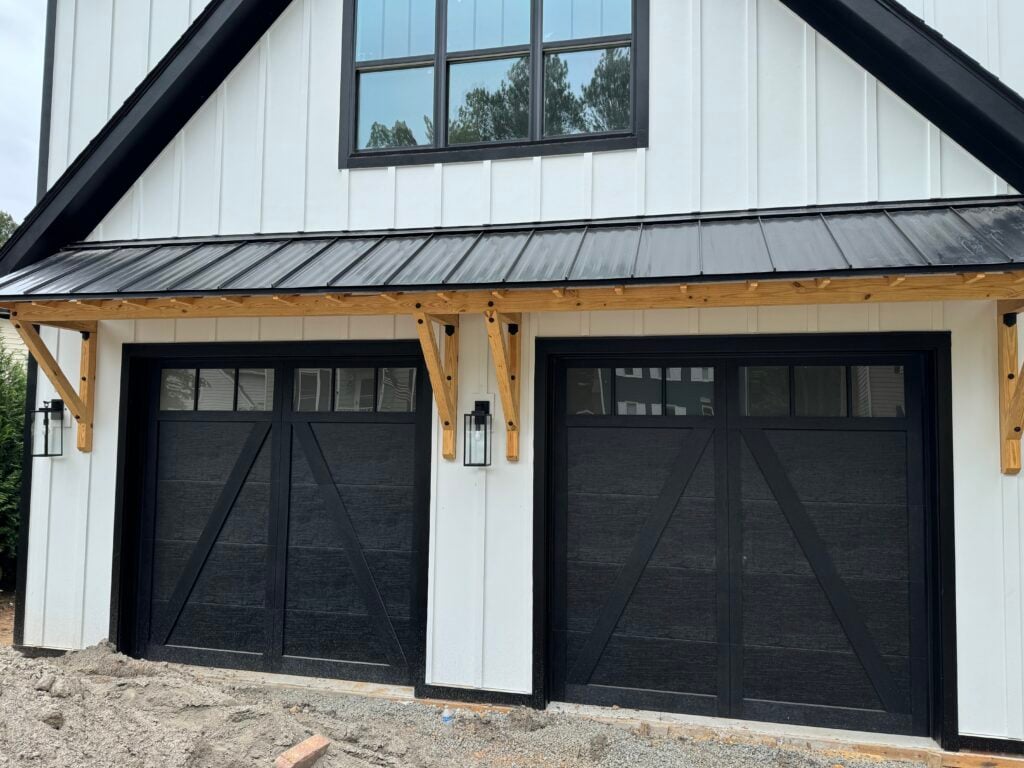 Two black carriage-style garage doors with upper windows on a white farmhouse